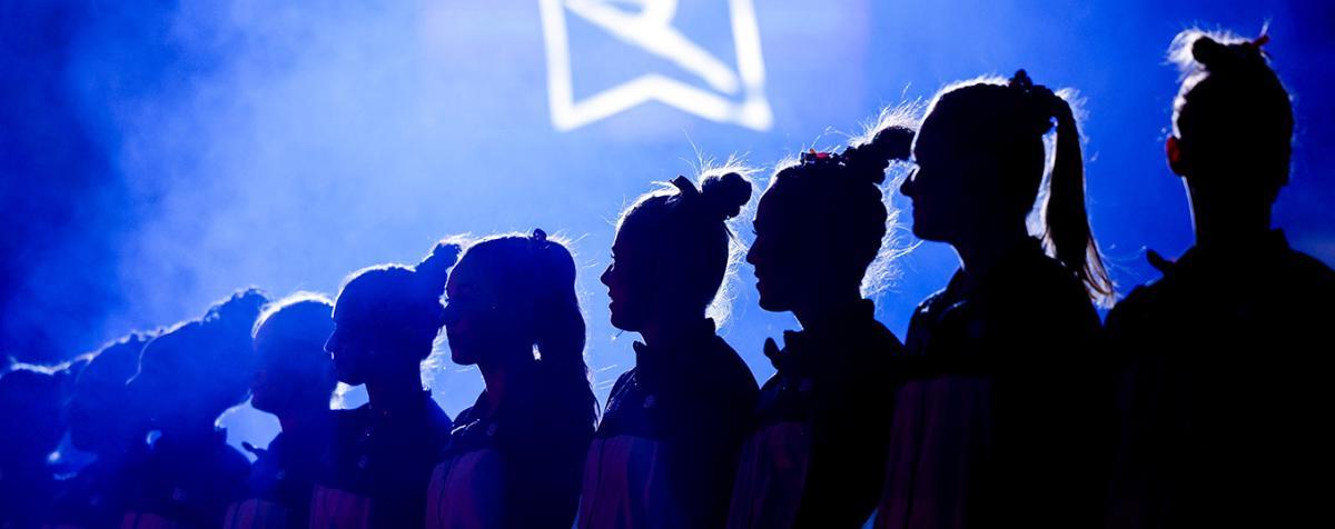 silhouetted gymnasts in a darkened arena